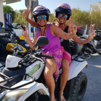 satisfied customers wearing pink clothes and helmets posing on a white quad in front of our office in perissa santorini