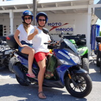 satisfied customers posing on a blue scooter in front of moto manos office in perissa santorini