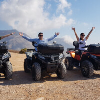 three friends on their quads rented from moto manos in perissa spreading their arms for photo on top of emboreio hill