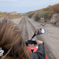 woman driving a red quad on santorini dirt road. photo taken by moto manos rentals in perissa santorini